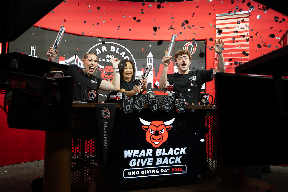Chancellor Joanne Li (center) celebrates Wear Black, Give Back, with two students at the UNO Television studio. All three individuals are shooting off confetti.